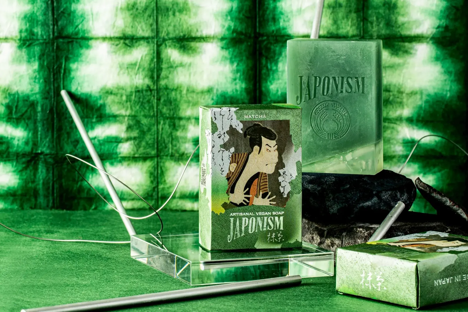 緑の絞り染めの布の前に置かれた、JAPONISMの情景 MATCHA の石鹸と包み紙